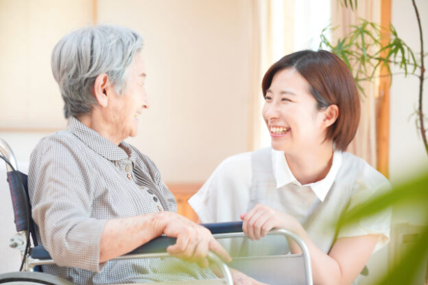 介護職員が高齢者と笑顔で交流している風景。室内での日常的なケアシーン。