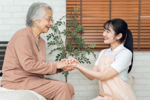 介護職員と高齢入居者が室内で植物を一緒に手入れしている交流風景。